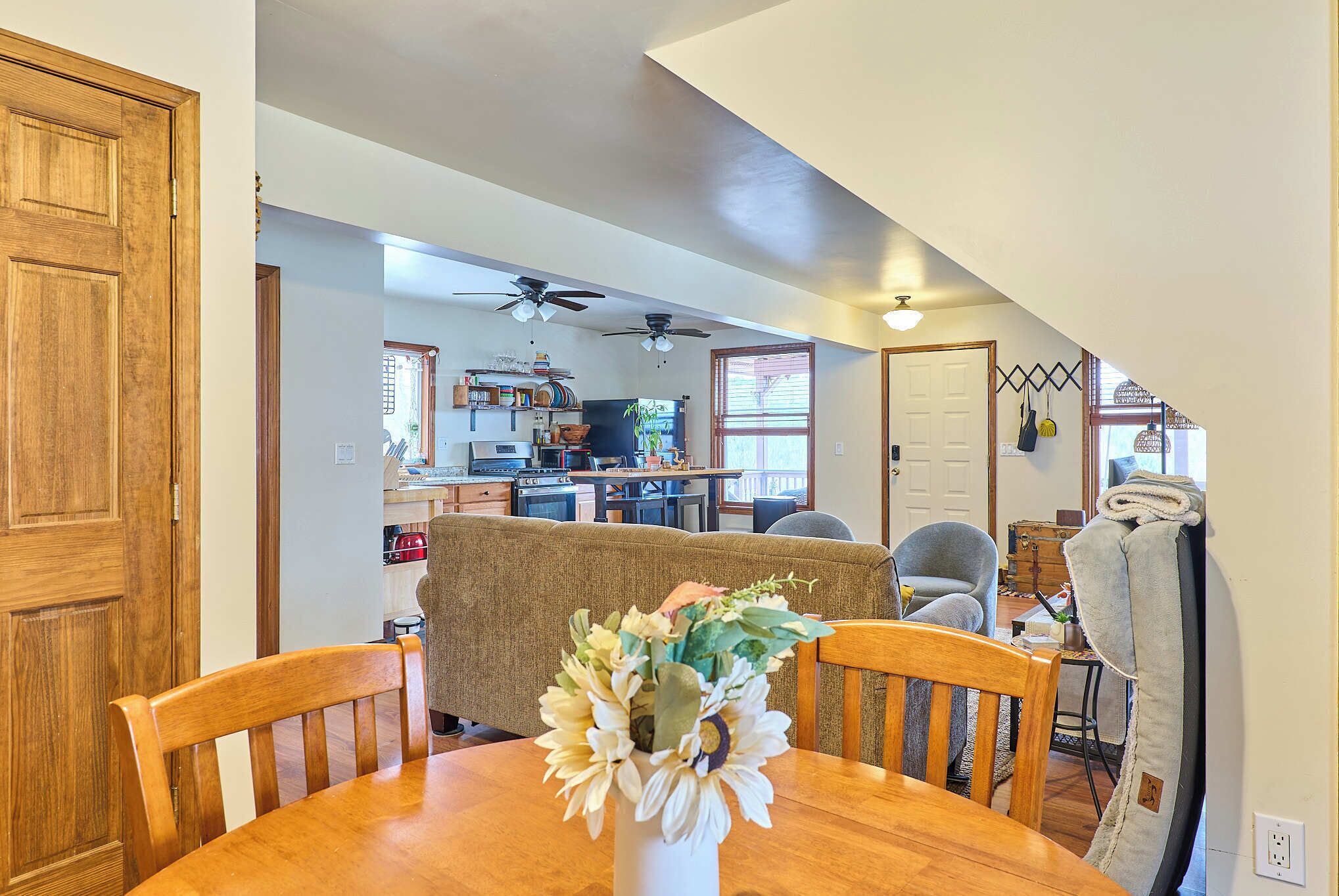 A dining area with a wooden table and chairs, a vase with flowers, and a kitchen in the background.