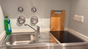 A stainless steel kitchen with a sink, stove, and wooden utensil drawer. - Cozy studio near university & hospital by CASTORA HOMES (Kassel)