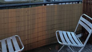 A balcony with two metal chairs, a wooden fence, and a view of multi-story buildings in the background. - Cozy studio near university & hospital by CASTORA HOMES (Kassel)
