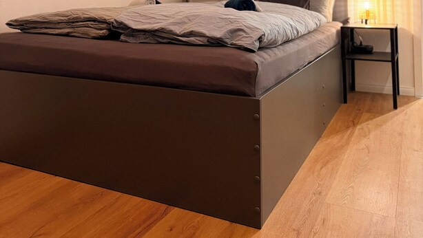 A bedroom with a bed, wooden floor, a nightstand, and a wall-mounted shelf. - Cozy studio near university & hospital by CASTORA HOMES (Kassel)