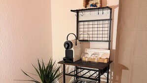 A corner kitchenette with a metal shelf unit holding a coffee maker, toaster, kettle, and a small plant. - Cozy studio near university & hospital by CASTORA HOMES (Kassel)
