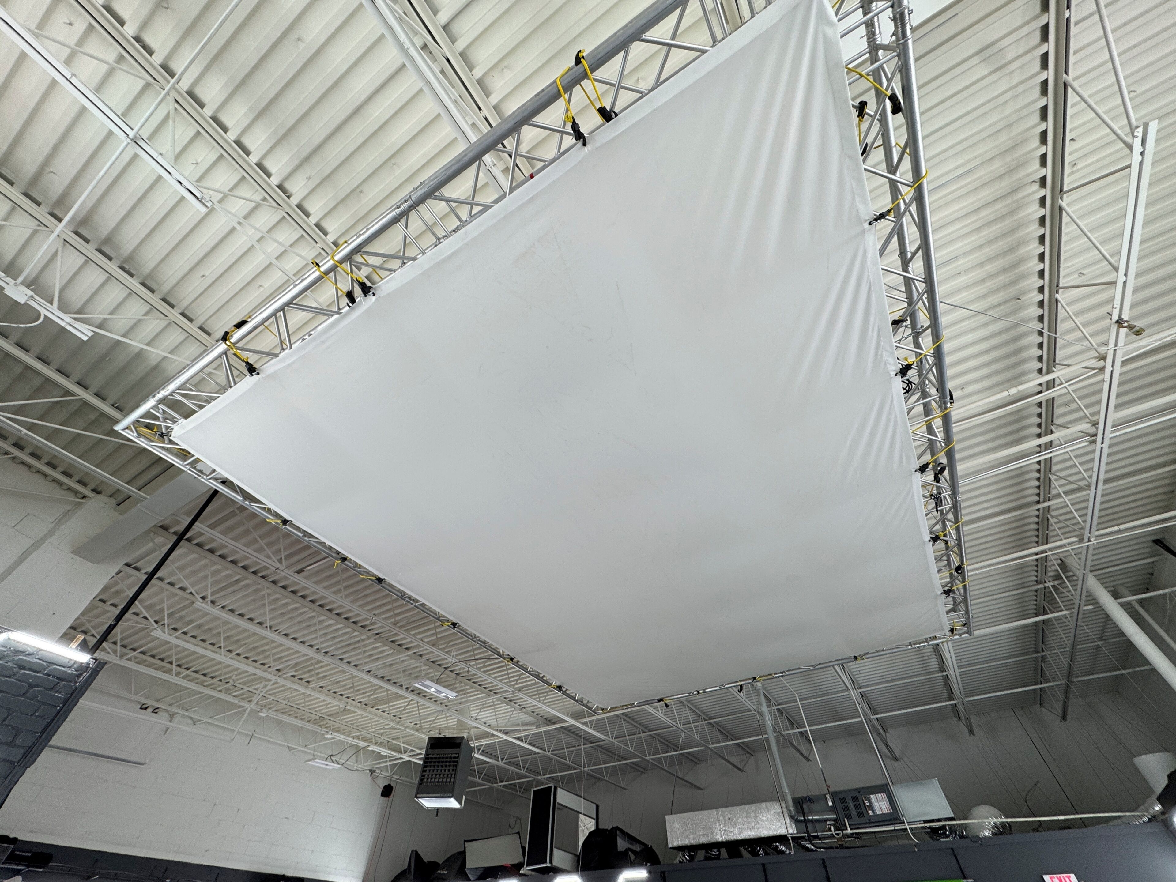 Een groot wit scherm, opgehangen aan een metalen constructie in een ruime industriële ruimte.