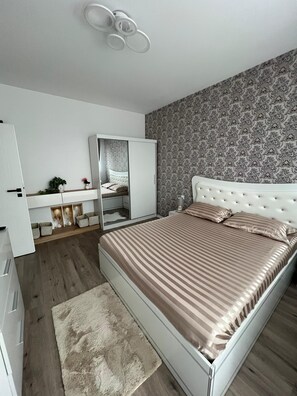 A bedroom with a bed, a wardrobe, a mirror, a vanity, and a patterned wall.