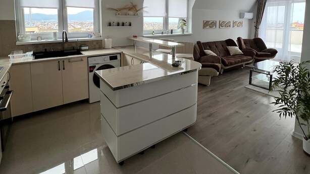 Una cocina moderna con una isla central, un área de comedor con sofá y ventanas grandes con vistas a la ciudad.