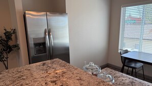 Una cocina con un refrigerador de acero inoxidable, encimera de granito, dispensador de agua y ventana con persianas.