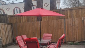 A patio with a table and chairs, a red umbrella, and a wooden fence.
