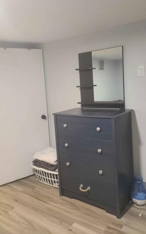 A dark-colored dresser with drawers and a mirror, a white door, a laundry basket, and a blue water dispenser.