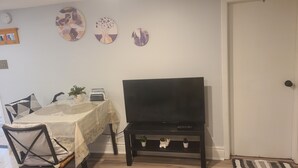 A living room with a TV on a stand, a dining table with chairs, and a door.