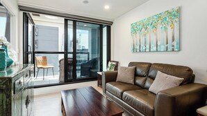 Un salon avec un canapé en cuir, une table basse en bois, un fauteuil en osier et une grande fenêtre donnant sur la ville.