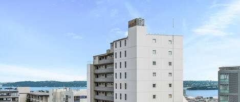 A multi-story residential building with balconies, a flat roof, and a view of a body of water.