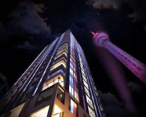 A high-rise building with illuminated windows and a prominent tower structure in the background. - Central 2BR Escape w Pool & Gym  Zodiak Stays (Auckland)
