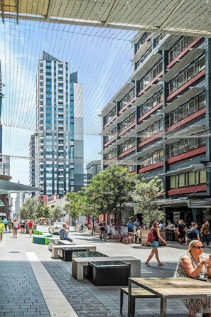 Un espace extérieur urbain aménagé avec des sièges, une promenade piétonne et des immeubles de grande hauteur en arrière-plan.