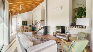 Un salon moderne comprenant un canapé, des fauteuils, un téléviseur et un escalier menant à un niveau supérieur.