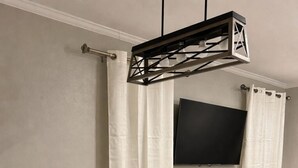 Ett modernt matområde med ett runt bord, fyra stolar, en tv som är monterad på väggen och ett litet sidobord med en växt.