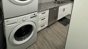 Ett kompakt kök med en tvättmaskin med frontmatning, en inbyggd diskmaskin och vita köksluckor.