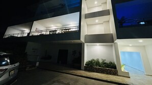 Un edificio moderno a più piani con balconi, una scala e un'auto parcheggiata di fronte.