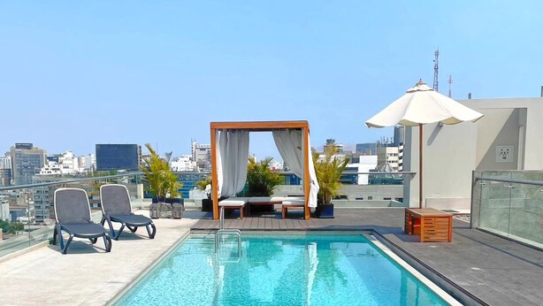 A rooftop pool with lounge chairs, a canopy, and a view of the cityscape. - Apartamento Moderno em Edifício de Luxo - 3 beds/3 baths (Miraflores)