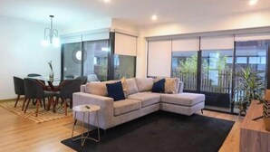 A modern living room with a sectional sofa, a dining table with chairs, and large windows with a view. - Apartamento Moderno em Edifício de Luxo - 3 beds/3 baths (Miraflores)