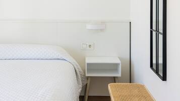 A minimalist room with a bed, a small white nightstand, a wicker side table, and a framed abstract artwork on the wall.