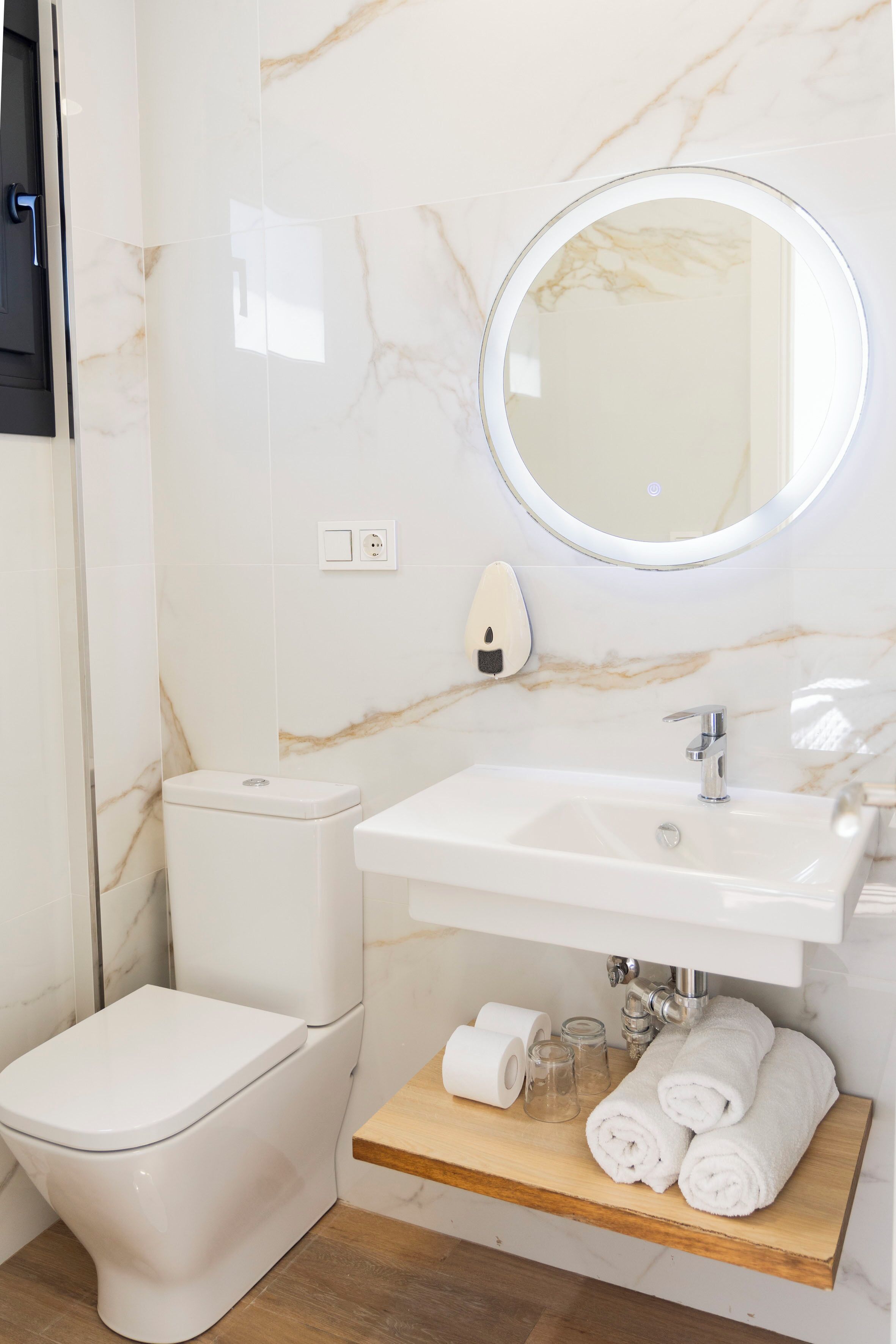 A bathroom with a toilet, sink, mirror, and a shelf with towels and toiletries.
