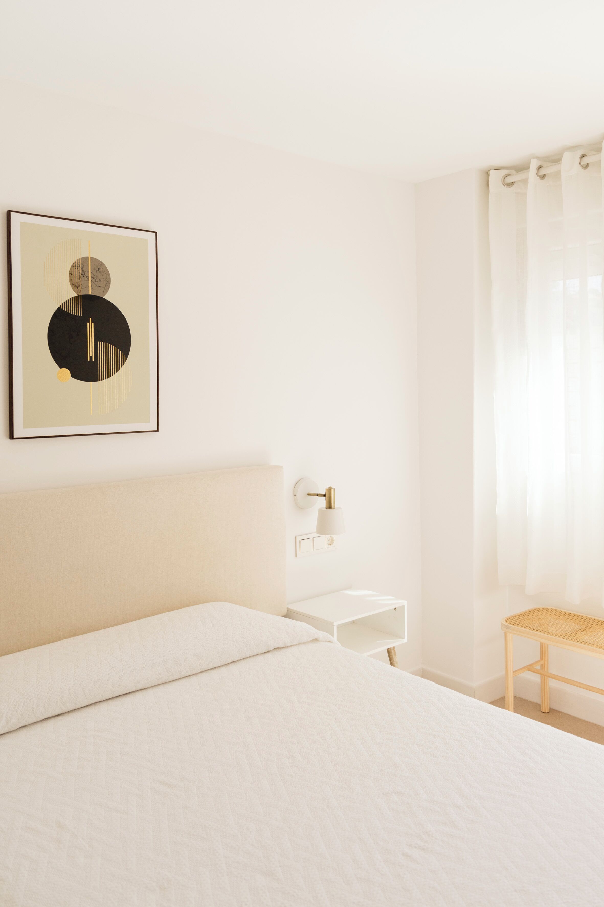 Ein schlicht eingerichtetes Hotelzimmer mit Bett, kleinem Schreibtisch, Wandlampe und einem gerahmten Bild.