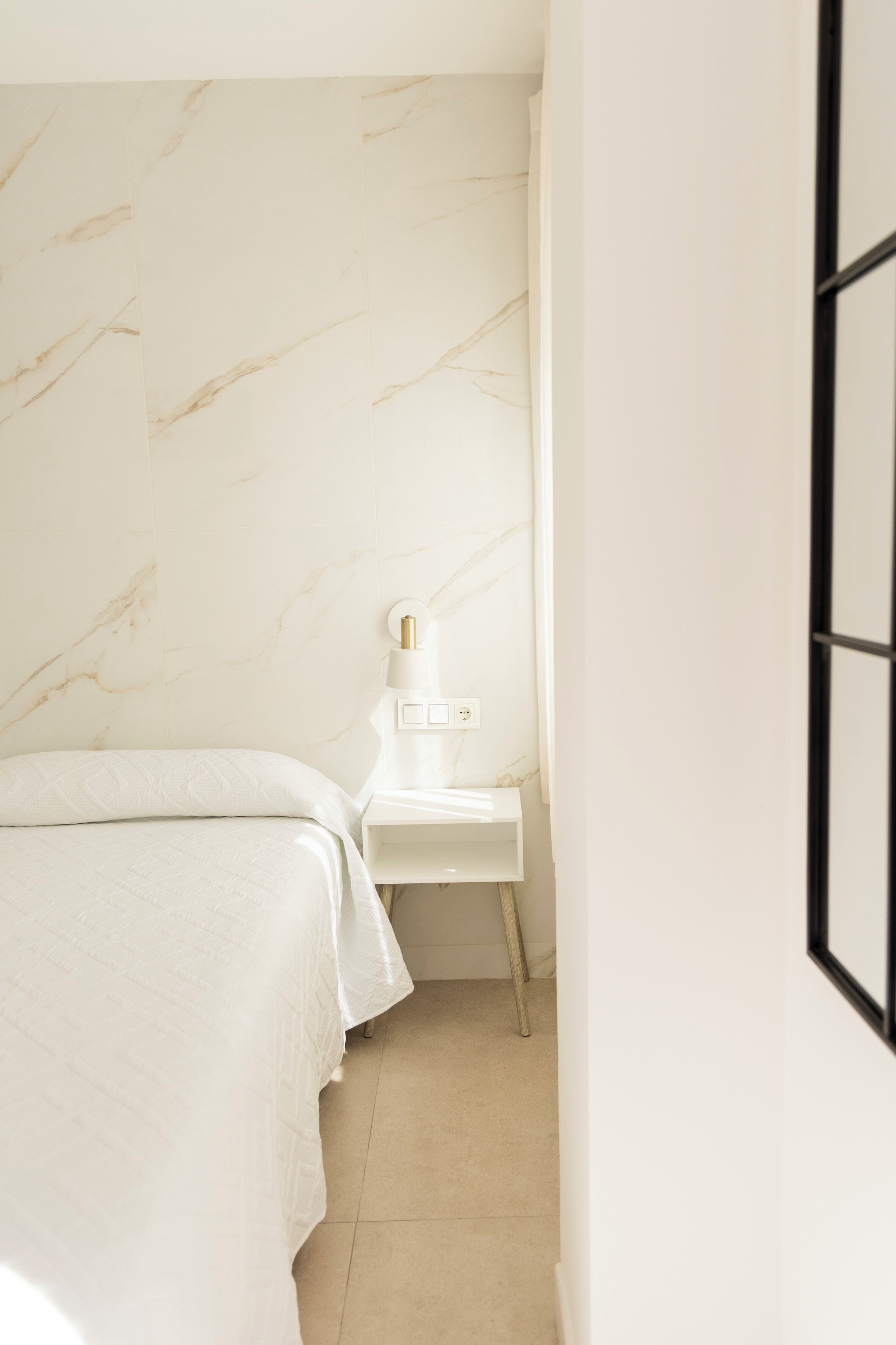 A bedroom with a bed, a nightstand, a wall-mounted lamp, and a framed picture on the wall.