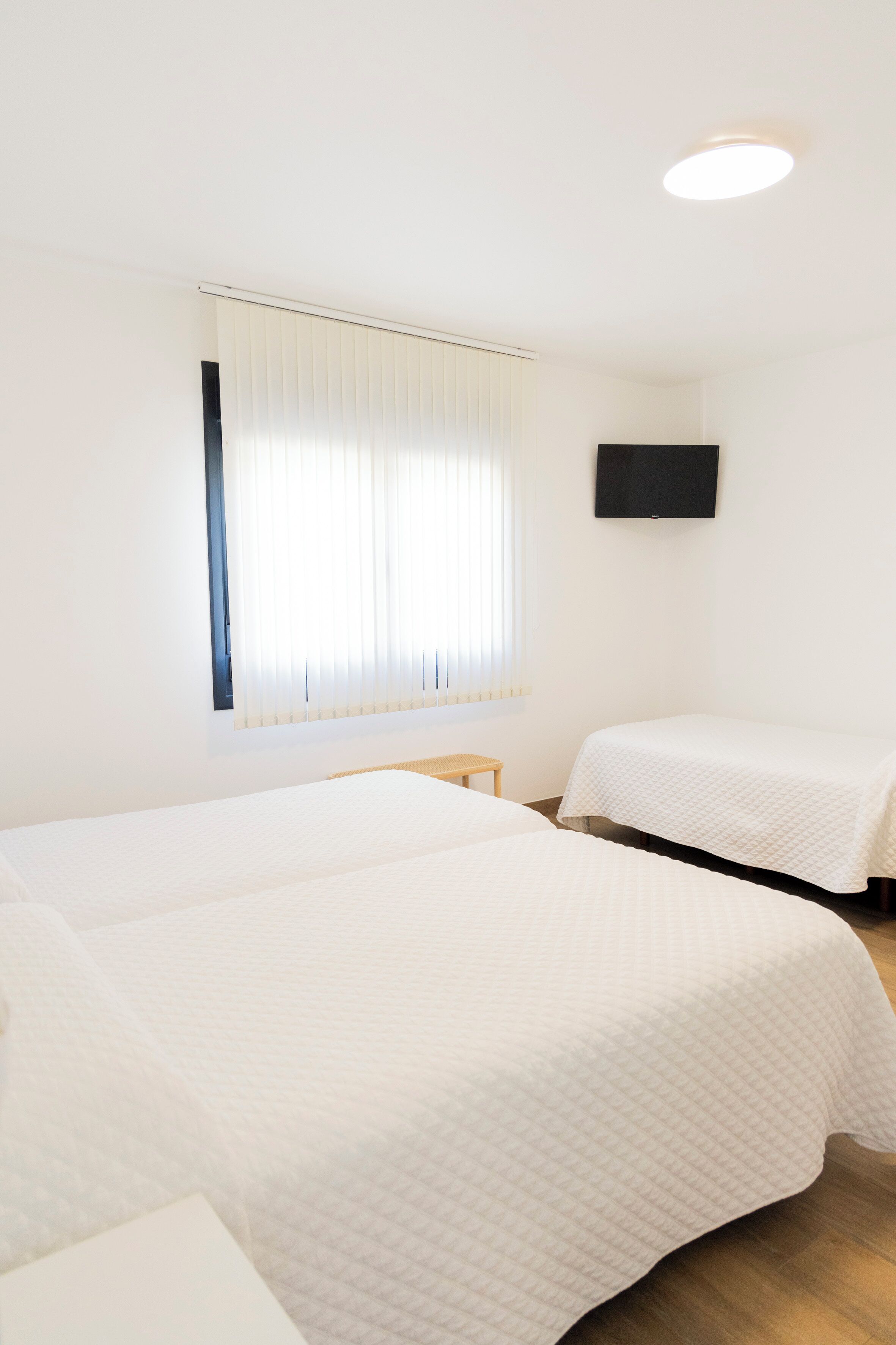 A hotel room with two beds, a television on the wall, and a window with blinds.