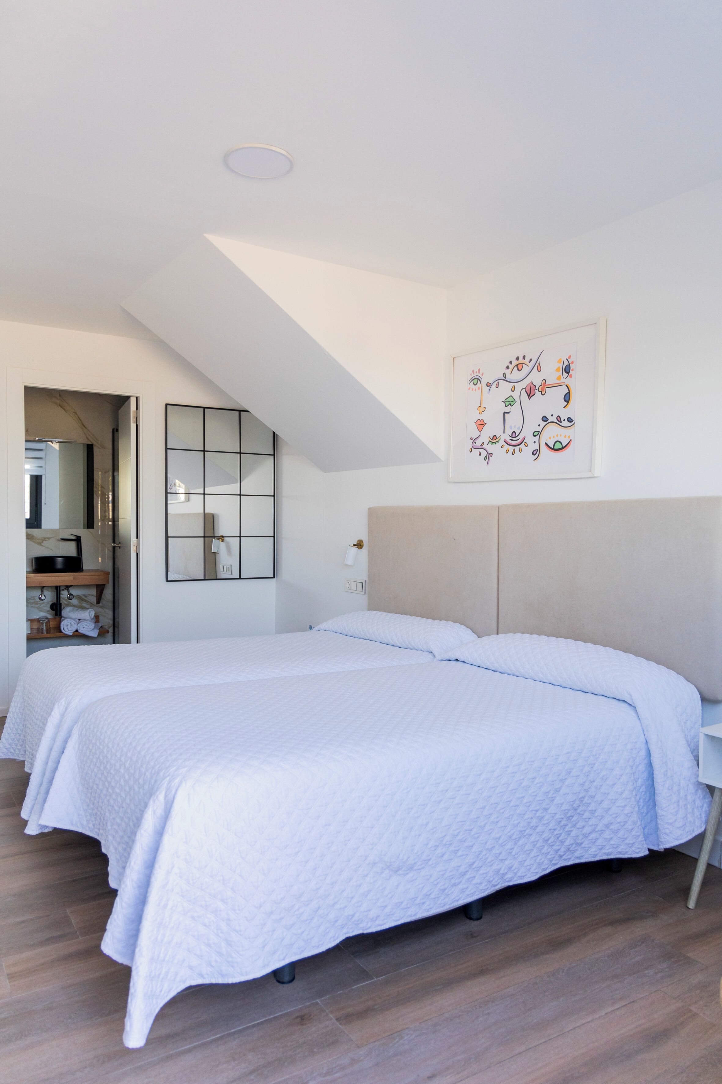 A bedroom with a large bed, a bedside table, a mirror, and a framed artwork on the wall.