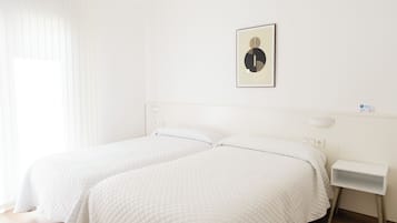 A room with two beds, a bedside table, a wall-mounted light, and a framed picture.