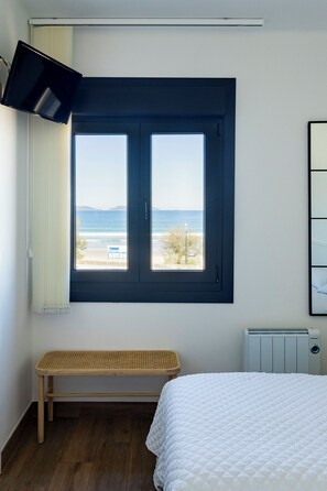 A bedroom with a large window, a bed, a bench, and a radiator. - hostal montevideo (Nigrán)
