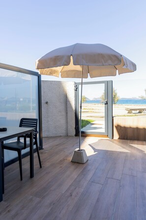 An open patio with a table and chairs, a beige umbrella, and a view of the sea. - hostal montevideo (Nigrán)