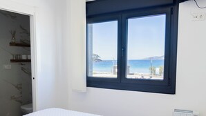 Une chambre à coucher avec un lit, une fenêtre donnant sur la mer, un radiateur et une porte menant à la salle de bain.