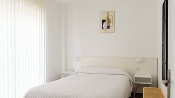 A hotel room with a bed, bedside tables, a wall-mounted artwork, and a window with blinds.
