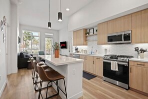 A modern kitchen with a central island, bar stools, a microwave, oven, and a TV mounted on the wall.