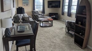 A living room with a sofa, armchair, coffee table, TV, and a surfboard display. - Spacious home with handicap ramp, boat parking,  a golf cart is also available (Sandusky)