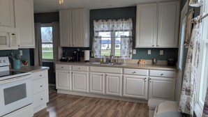 A kitchen with white cabinets, a stove, a sink, and a window with curtains. - Spacious home with handicap ramp, boat parking,  a golf cart is also available (Sandusky)