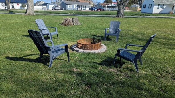 A grassy outdoor area with a fire pit and four Adirondack chairs. - Spacious home with handicap ramp, boat parking,  a golf cart is also available (Sandusky)