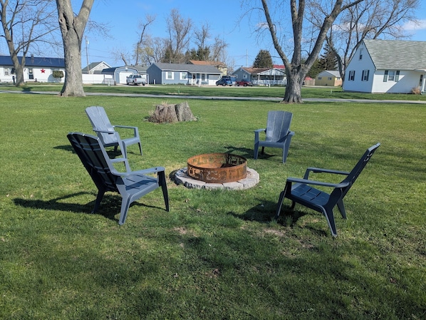 A grassy outdoor area with a fire pit and four Adirondack chairs.