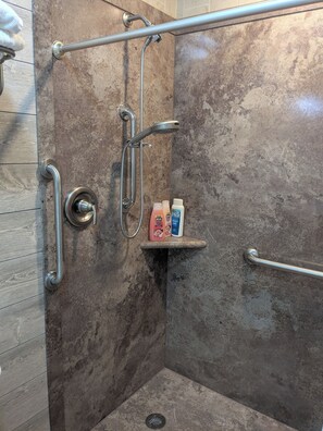 Un espace douche équipé d’une barre d’appui, d’une étagère pour les articles de toilette et d’un mur à surface texturée.