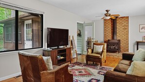 A living room with a television, leather chairs, a fireplace, and a large window. -  Mountain lodge w/ cozy fall vibes! Slps 10, Wooded views, Hot tub & fire pit (McGaheysville)