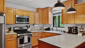 A kitchen with wooden cabinets, stainless steel appliances, a large island, and pendant lighting. -  Mountain lodge w/ cozy fall vibes! Slps 10, Wooded views, Hot tub & fire pit (McGaheysville)
