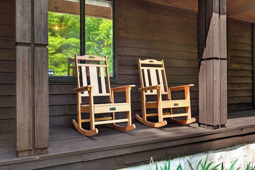 Two rocking chairs on a wooden porch with a window overlooking greenery.
