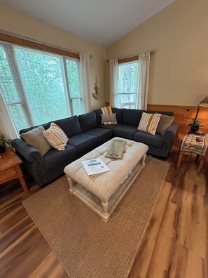 A living room with a sectional sofa, a coffee table, and a wooden floor. - "West View Cabins" on Ostego Lake - Cabin #1 - Waterfront and on Trail 7 (Gaylord)