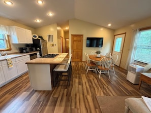 A modern kitchen with a central island, white cabinetry, and a dining area with a wooden table and chairs. - "West View Cabins" on Ostego Lake - Cabin #1 - Waterfront and on Trail 7 (Gaylord)