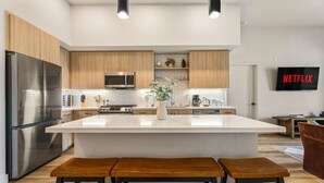 Une cuisine moderne dotée d’un îlot central, de meubles en bois, d’appareils électroménagers en acier inoxydable et d’un téléviseur avec accès à Netflix.