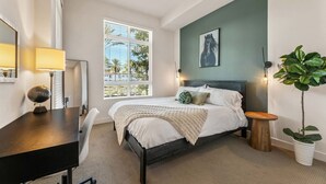 Une chambre à coucher avec un lit, une table de chevet, une lampe, une fenêtre et une plante.