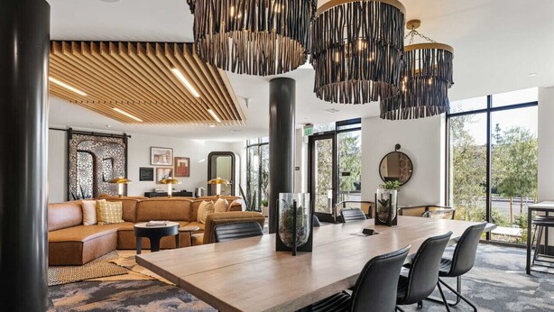 Un intérieur moderne avec une grande table à manger en bois, des chaises noires, un canapé et une grande fenêtre offrant une vue dégagée.