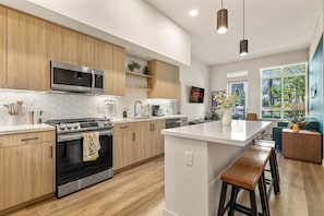 Une cuisine moderne avec des meubles en bois, un îlot central, des appareils électroménagers en acier inoxydable et une vue sur l’extérieur.