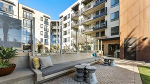 Un espace de détente extérieur moderne, avec un canapé et des tables en pierre, entouré d’un immeuble à plusieurs étages doté de balcons.