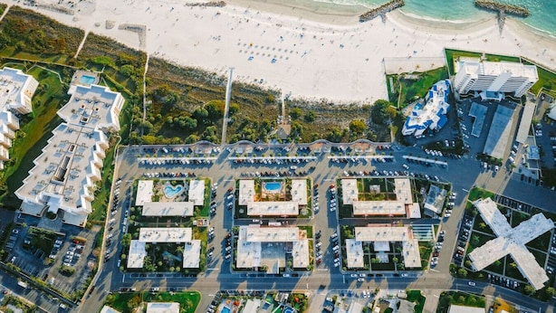 Luchtbeeld van een kustgebied met een strand, een parkeerplaats en moderne gebouwen.